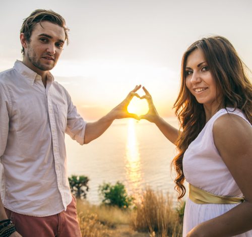 Couple in love kissing at sunset - Lovers on a romantic date outdoors making a heart shape with hands